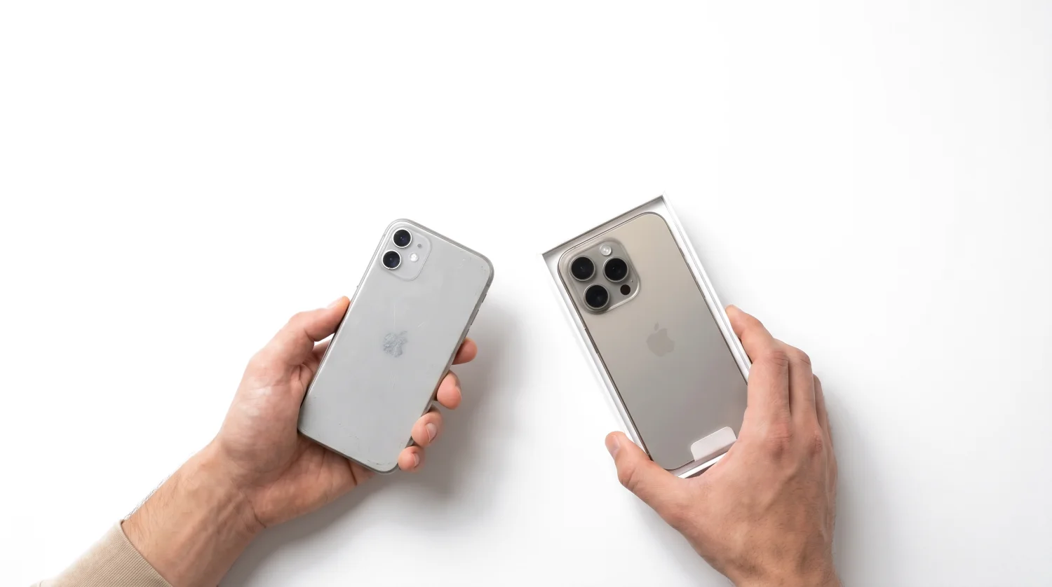 Eine Hand reicht ein altes Smartphone, die andere hält ein neues Gerät in der Verpackung